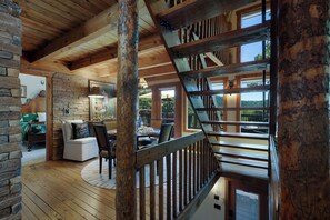 Ein Holzinnenraum mit einer Treppe, einem Essbereich mit Stühlen und einem Tisch sowie Blick durch große Fenster.