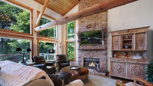 A cozy living room with a fireplace, large windows, and rustic wooden beams. - Chalet Lumiere - Big Canoe, GA (Jasper)