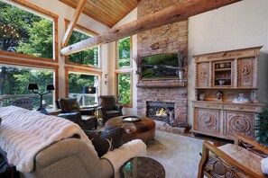 A cozy living room with a fireplace, large windows, and rustic wooden beams. - Chalet Lumiere - Big Canoe, GA (Jasper)