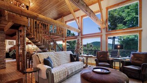 A spacious living area with a wooden staircase, a sofa, leather chairs, and large windows offering a view of the outdoors. - Chalet Lumiere - Big Canoe, GA (Jasper)