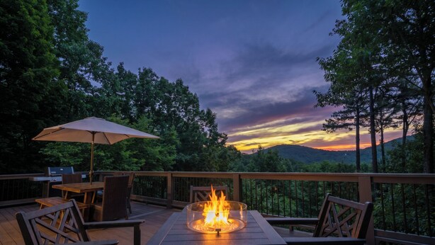 A deck with a fire pit, outdoor furniture, and a view of the sunset over a forested landscape. - Chalet Lumiere - Big Canoe, GA (Jasper)