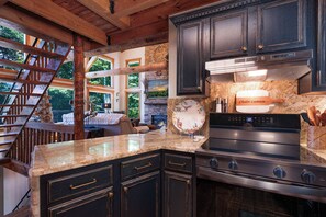 A kitchen with dark cabinets, a stainless steel stove, and a granite countertop. - Chalet Lumiere - Big Canoe, GA (Jasper)