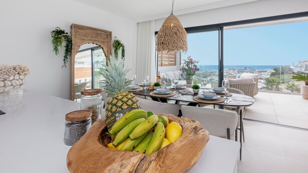 A modern dining area with a table set for two, a pineapple centerpiece, and a view of the ocean. - NEW!!! Sea Views, Beach, Pools, and Golf at La Cala Mijas—One Heights Apartment (Mijas)