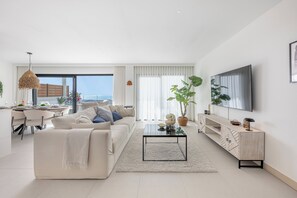 Ein modernes Wohnzimmer mit einer Couch, einem Couchtisch, einem Fernseher und einem Essbereich mit Tisch und Stühlen.