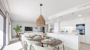 A modern kitchen with a central island, white cabinetry, and a dining area with a dark wood table and white chairs. - NEW!!! Sea Views, Beach, Pools, and Golf at La Cala Mijas—One Heights Apartment (Mijas)