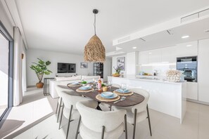 Eine moderne Küche mit einer zentralen Kochinsel, weißen Schränken und einem Essbereich mit einem dunklen Holztisch und weißen Stühlen.