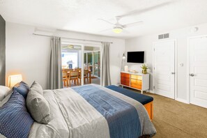 Ein Hotelzimmer mit Bett, Schreibtisch, Sessel, Fernseher und einer Schiebetür zum Balkon.