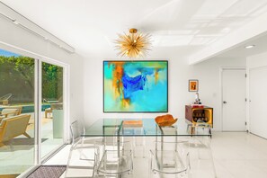 A modern dining area with a glass table, clear chairs, a large abstract painting, and a unique ceiling light fixture. - 25% Off Sept 11-13 Great 4 Families -Pool, Jacuzzi (Palm Springs)