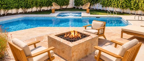 A swimming pool with a fire pit and lounge chairs.