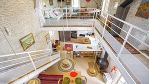 Ein mehrgeschossiges Interieur mit Küche, Essbereich und Wohnraum, das eine Steinwand, weiße Geländer und ein Schlafzimmer im oberen Bereich zeigt.