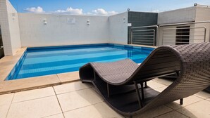 Ein Swimmingpool mit Fliesenbelag, einer Liege und einem Metallgeländer.