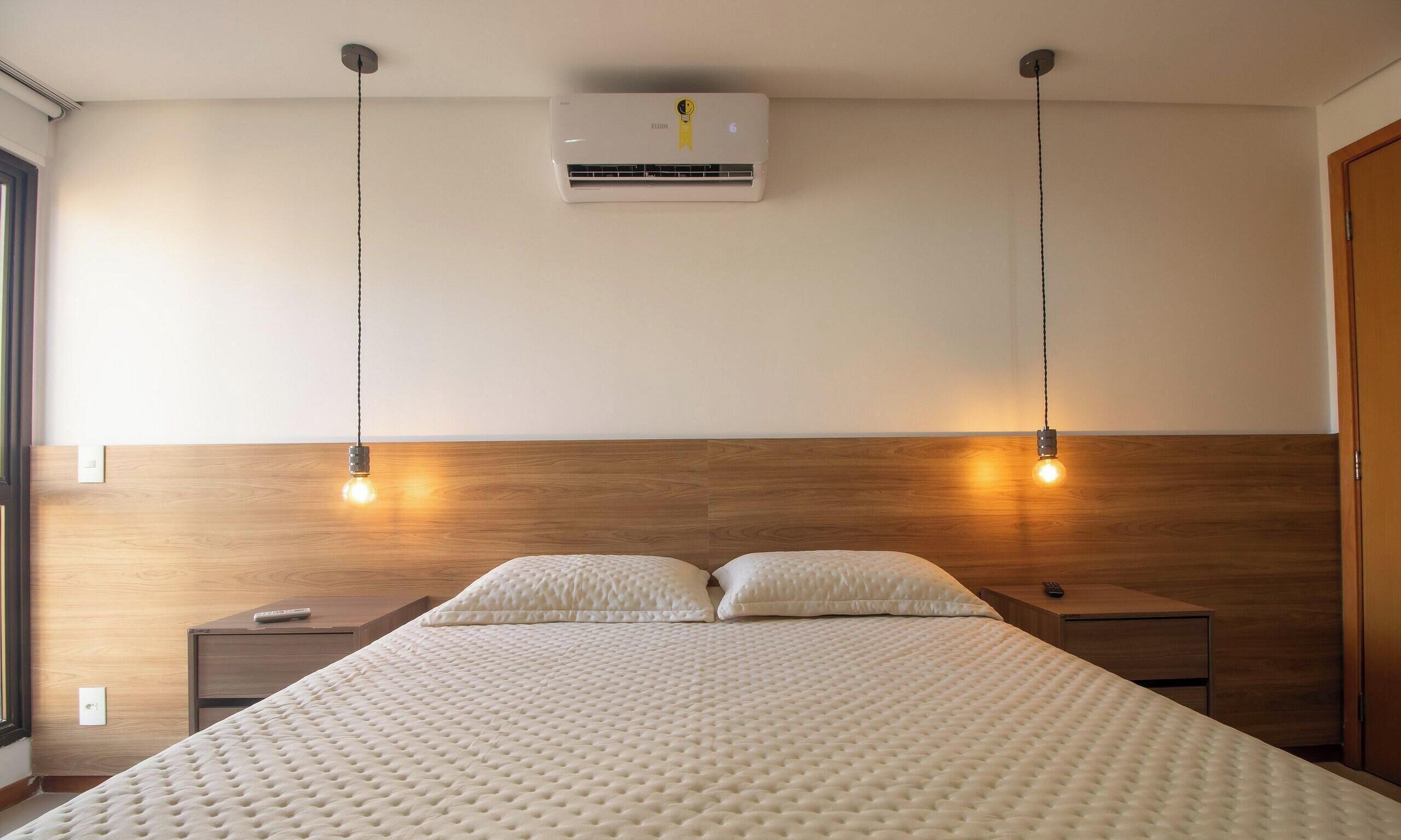 A modern bedroom with a wooden headboard, a central air conditioning unit, and two bedside lamps.