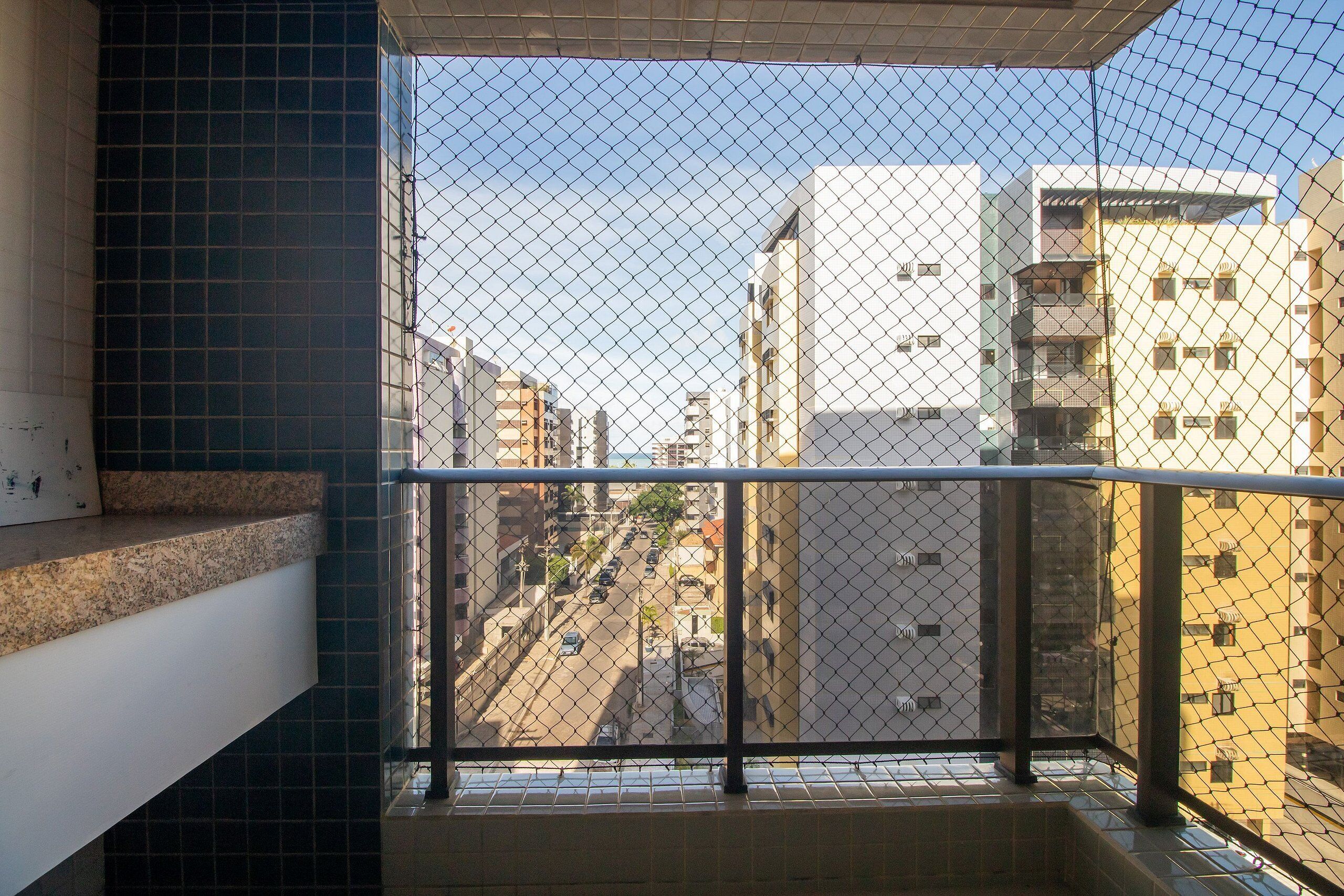 A balcony with a metal railing, a tiled floor, and a view of a city street with buildings.