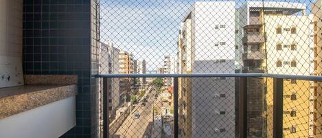 A balcony with a metal railing, a tiled floor, and a view of a city street with buildings.