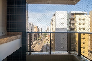 Un balcón con barandilla de metal, suelo de baldosas y vista a una calle urbana con edificios.