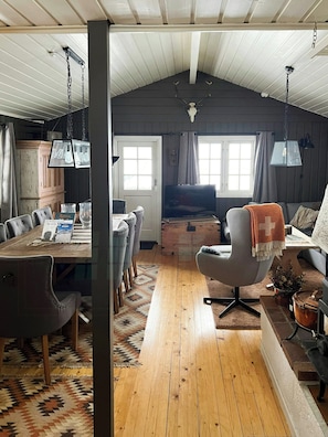 A cozy room with a wooden dining table, chairs, a sofa, a television, and a fireplace. - Mountain cabin by ski trails in southern Blefjell (Kongsberg)