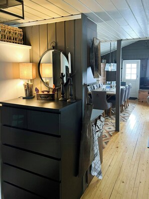 A modern kitchen with a dark countertop, a hanging light fixture, and a dining area with a wooden table and chairs. - Mountain cabin by ski trails in southern Blefjell (Kongsberg)