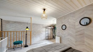Un dormitorio con cama, escritorio, silla, lámpara de pie, espejo y pared con motivo de espiga.