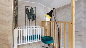 Una habitación con una cuna blanca, una silla color turquesa, una lámpara negra y paredes de madera.