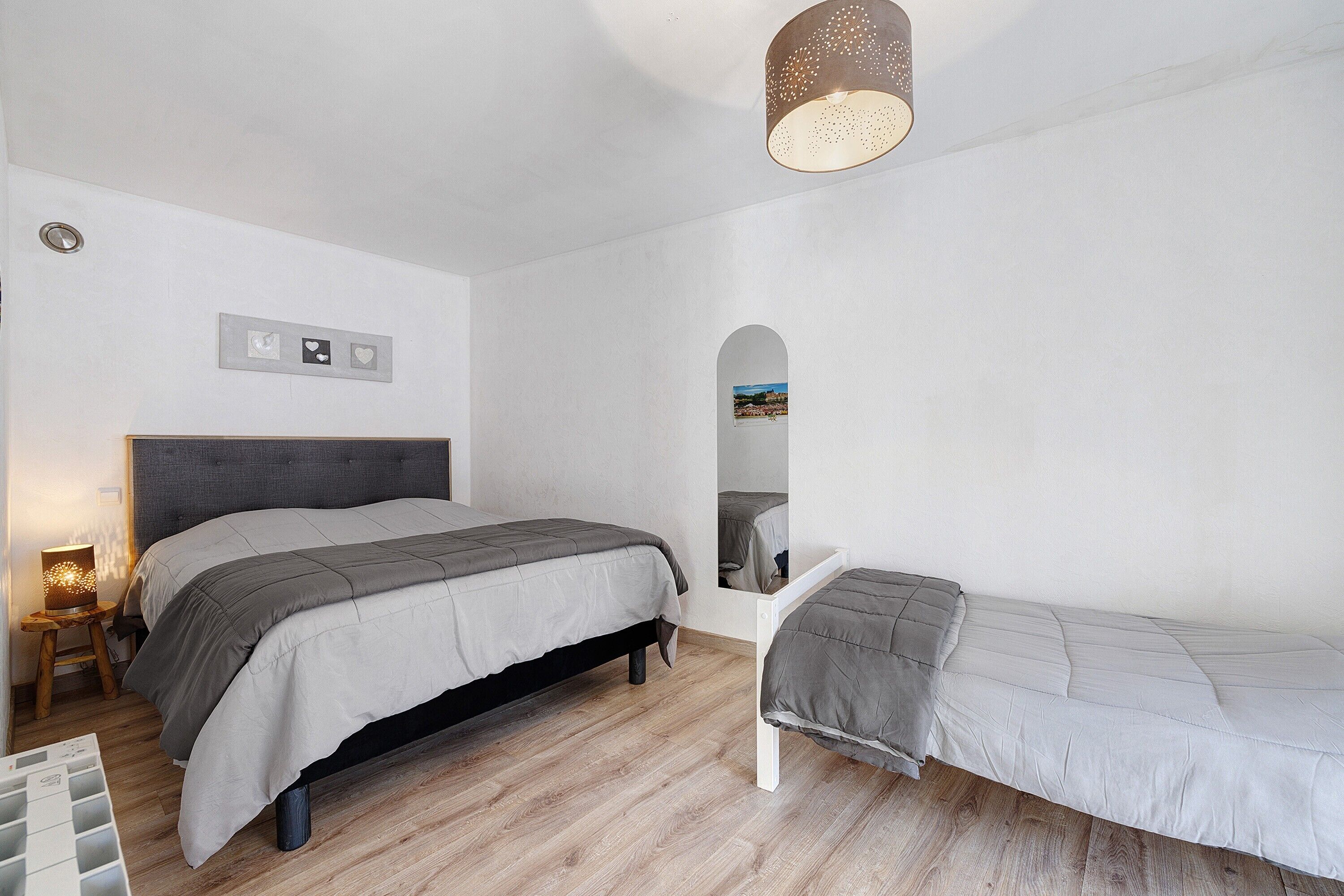 Une chambre à coucher comprenant un lit, un banc, une table de chevet, une lampe et un miroir.
