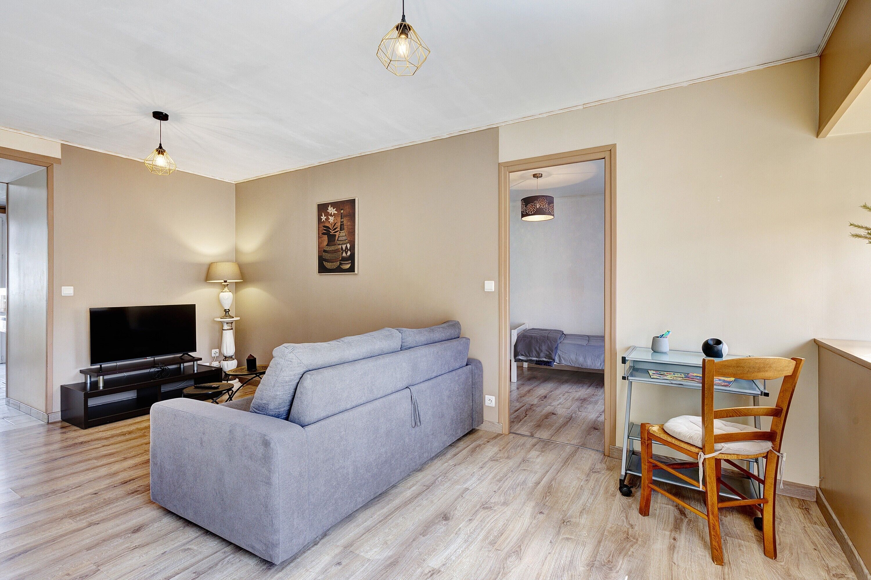 Ein Wohnzimmer mit einer Couch, Fernseher, Lampe und einem Holzsessel.