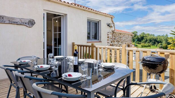 Un comedor al aire libre con una mesa preparada para cuatro personas, una botella de vino y una parrilla.