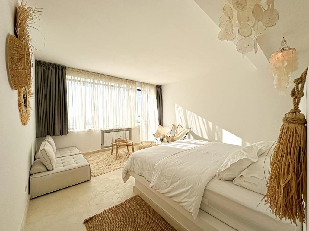 Un dormitorio con cama, sofá, sillón y un amplio ventanal.