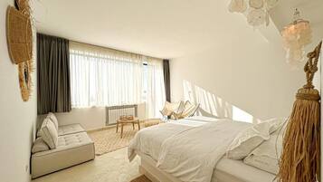 Un dormitorio con cama, sofá, sillón y un amplio ventanal.