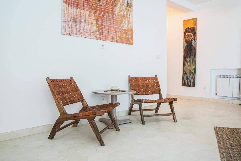 A room with two wooden chairs, a small round table, and two artworks on the walls.