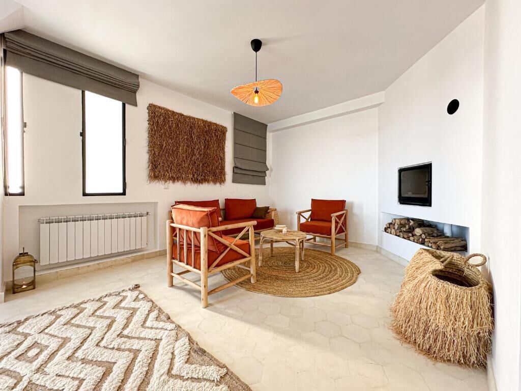 Un salon comprenant un ensemble de canapés, une table basse, un luminaire suspendu, une cheminée et un panier en osier.