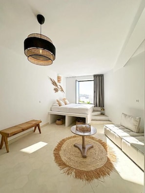 A modern bedroom with a bed, a bench, a round table, and a hanging light fixture. - Villa Le Belvedere (Tangier)