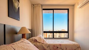Una camera d'albergo con due letti, una finestra vista città, una lampada e un quadro appeso al muro.