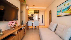 Un soggiorno moderno con una TV a schermo piatto, un divano, un'area pranzo con sedie e una cucina sullo sfondo.