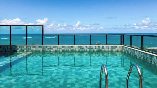 Cielo azzurro limpido, piscina con piastrelle a scacchi e vista sull'oceano.