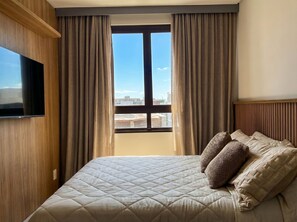 Een hotelkamer met een bed, gordijnen, een televisie en een raam met uitzicht op de stad.