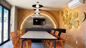 Un espace de repas moderne avec une longue table, des chaises en osier, un téléviseur à écran plat et un décor mural original.