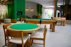 Een biljarttafel met stoelen, een groene wand en een plant.