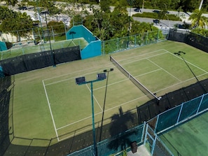 Ein Tennisplatz mit Netz, umgeben von einem Zaun und Bäumen im Hintergrund.