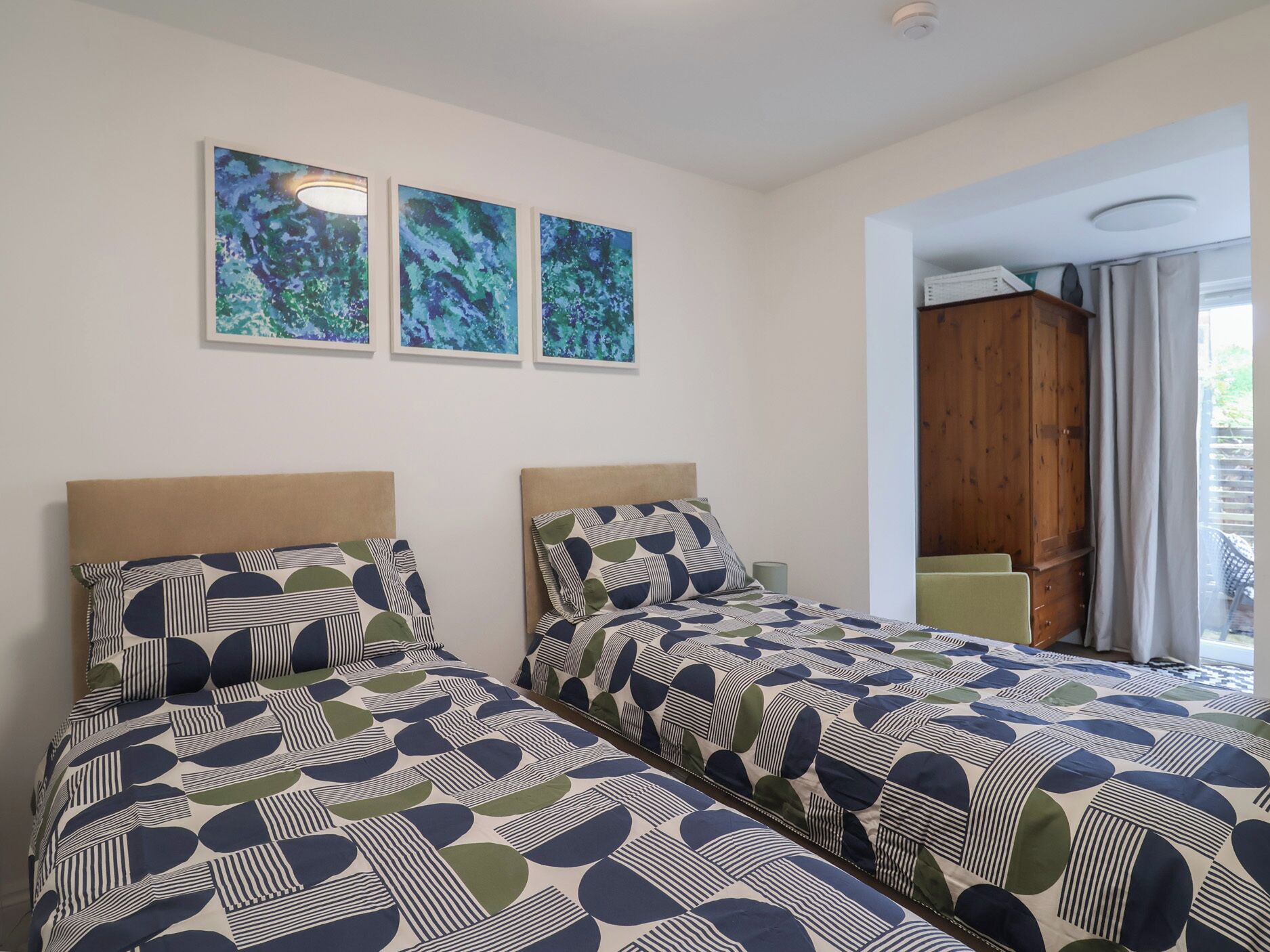 Una habitación con dos camas, un armario de madera y una ventana con cortinas.