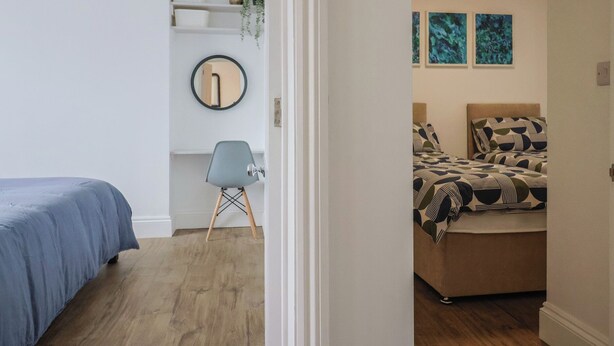 Un dormitorio con cama, una silla, un estante con cestas de almacenamiento y un espejo.