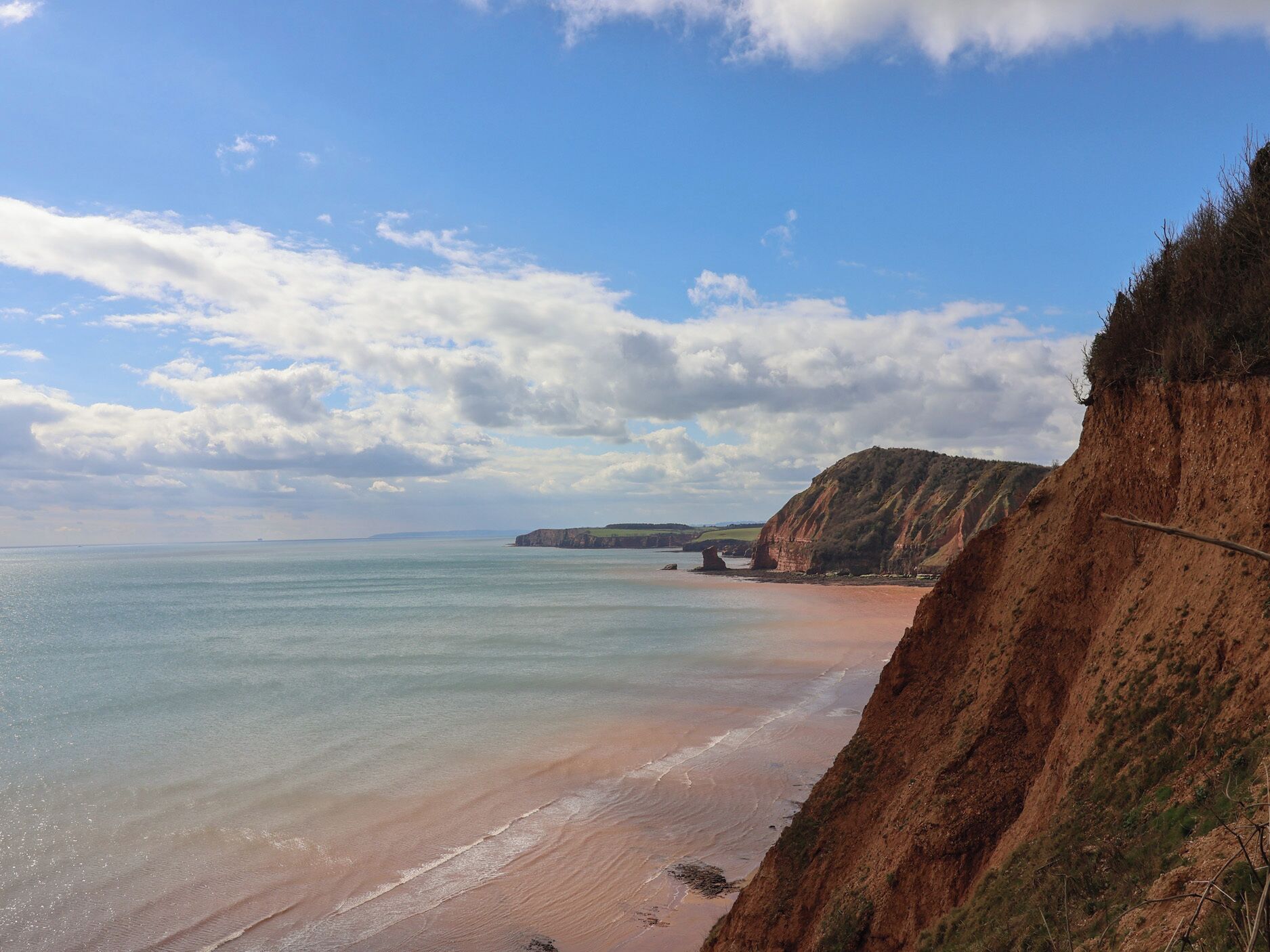 A coastal landscape with cliffs, a beach, and a clear sky.