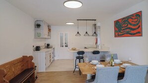 Una cocina moderna con armarios blancos, una zona de comedor con mesa de madera y sillas azules, y un banco.