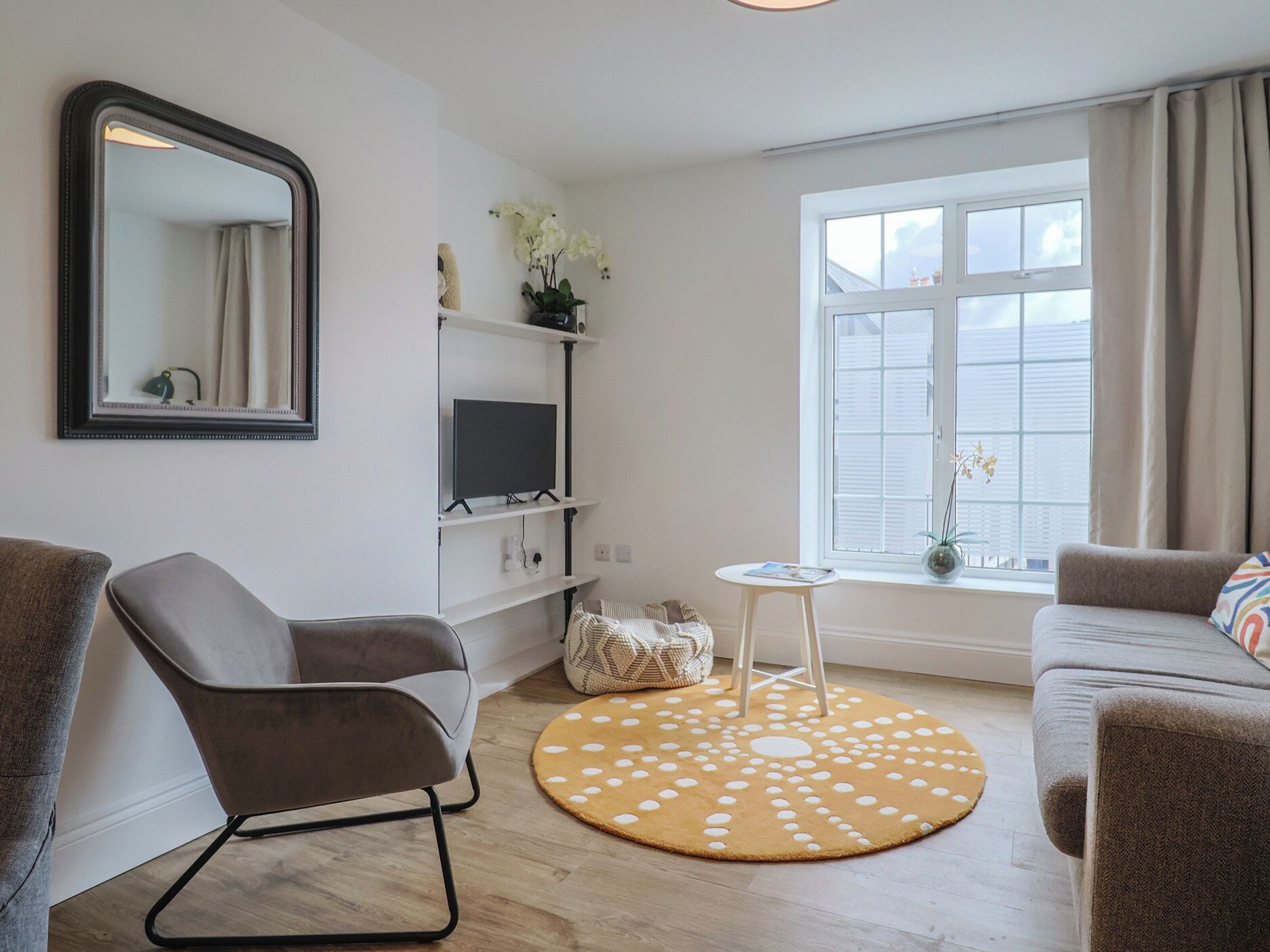 Una sala de estar con sofá, sillón, televisor y un tapete redondo.