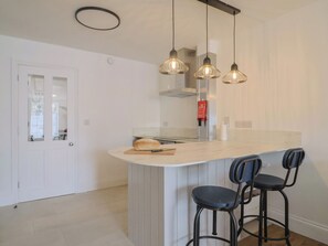 Una cocina moderna con una isla central, taburetes de bar, iluminación colgante y una puerta blanca.
