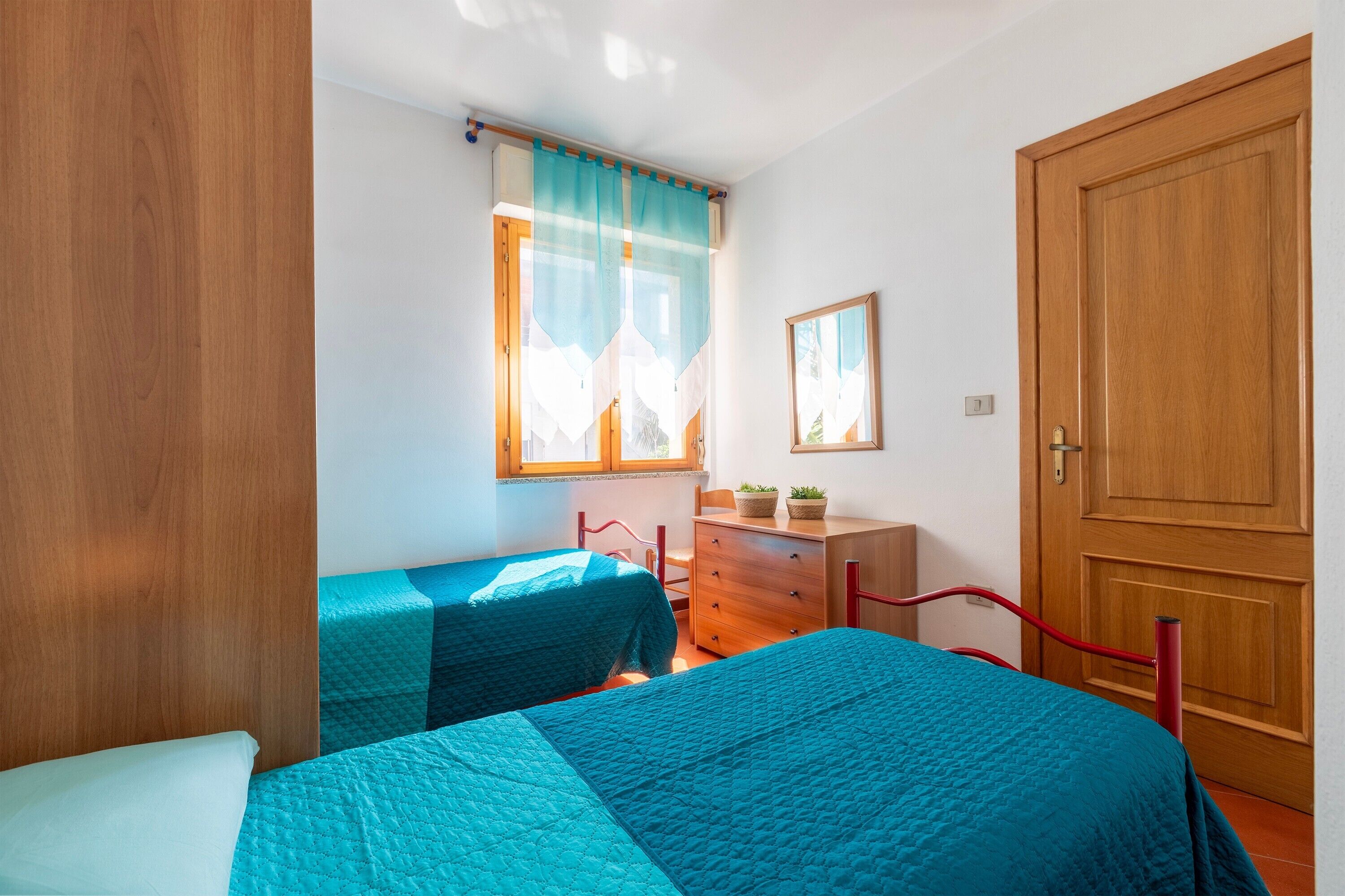 A bedroom with two beds, a wooden wardrobe, a dresser, a window with curtains, and a door.