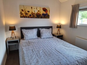 Een slaapkamer met een bed, twee nachtkastjes met lampen, een aan de muur hangend schilderij en een raam met gordijnen.