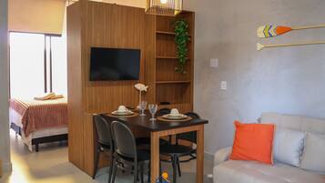 A compact living space with a dining area, a TV mounted on the wall, a plant, and a couch with an orange pillow.