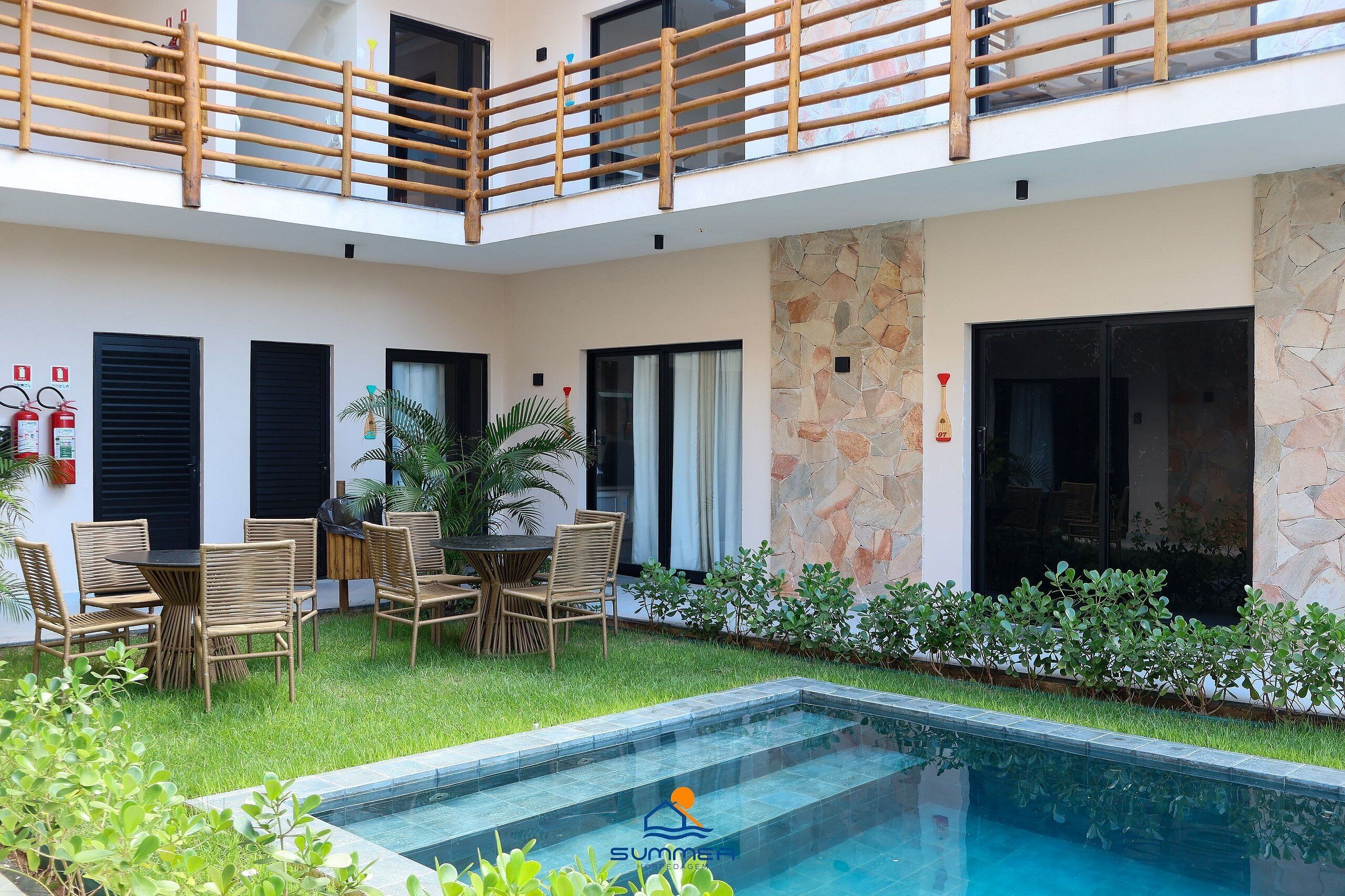 Uma área externa moderna com piscina, conjunto de jantar e parede de pedra.