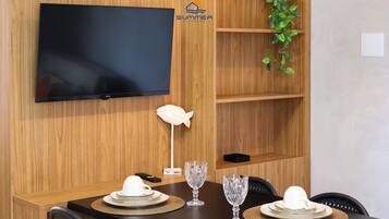 A dining area with a flat-screen TV mounted on a wooden wall, a white fish sculpture, and a potted plant.