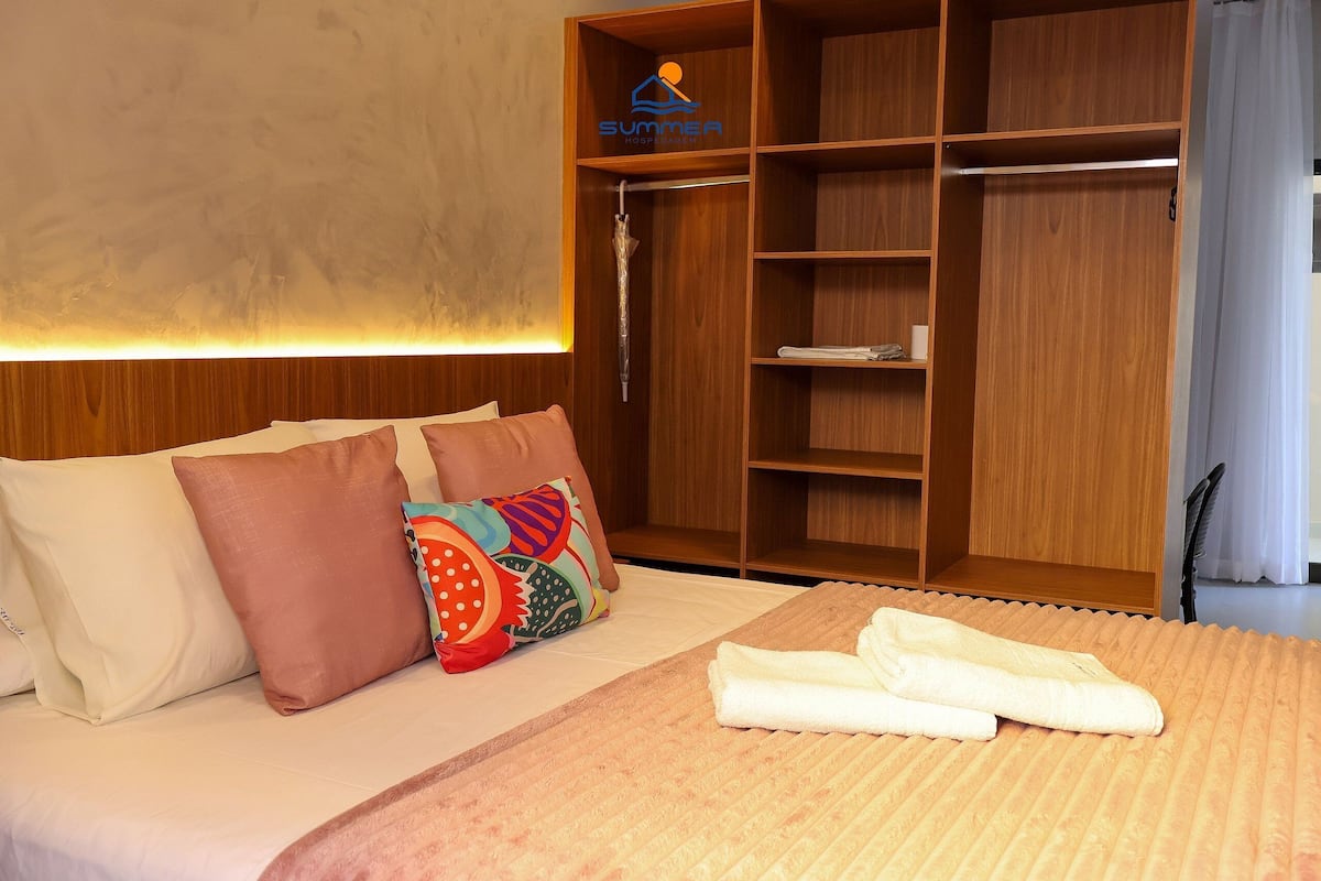 Una habitación de hotel con cama, almohadas, una toalla, armario y un logotipo en la pared.